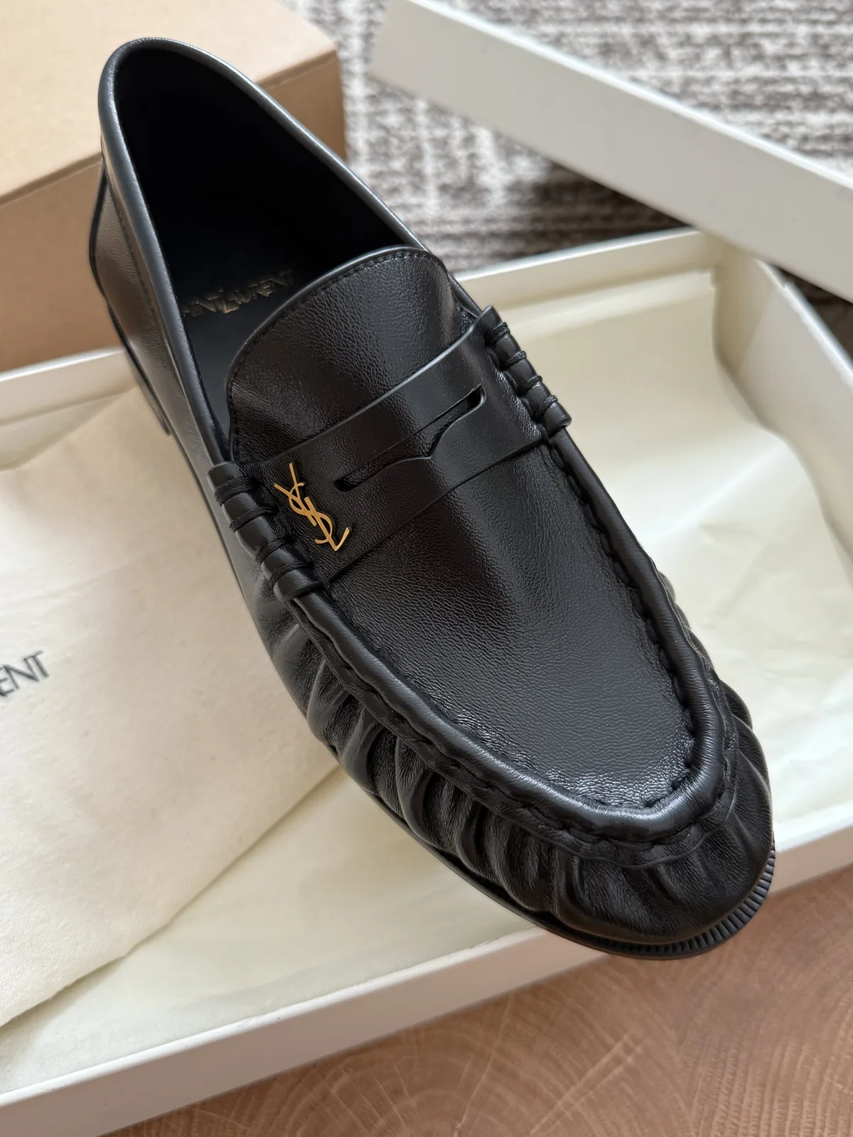 Black loafer with a rounded toe, gathered apron seam and a small gold tone detail